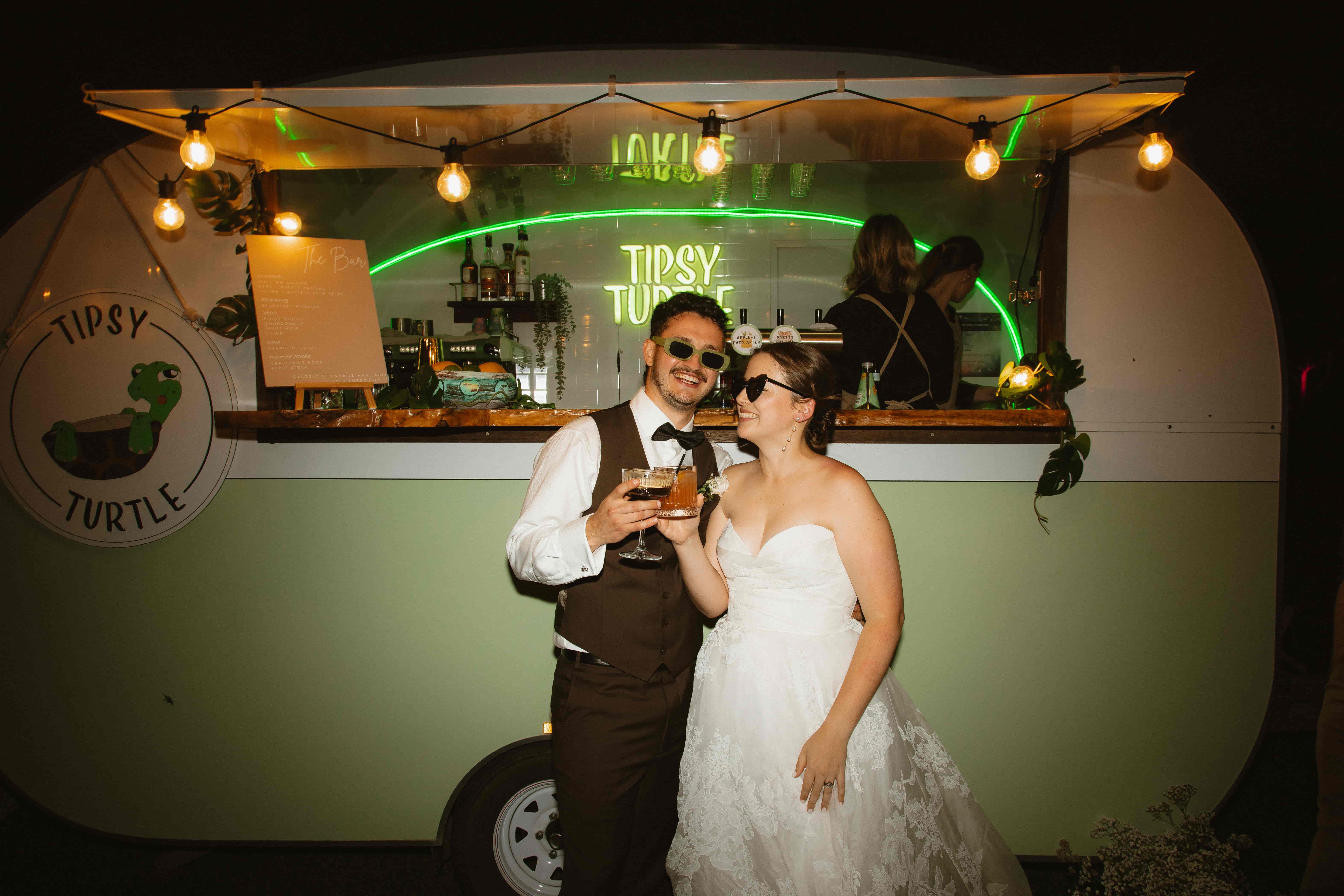 Newlyweds standing in front of the Tipsy Turtle mobile bar holding cocktails